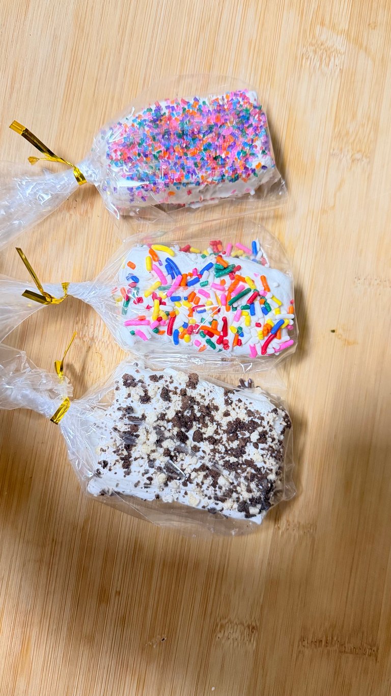 Three decorated cookies in plastic bags with gold twist ties on a wooden surface