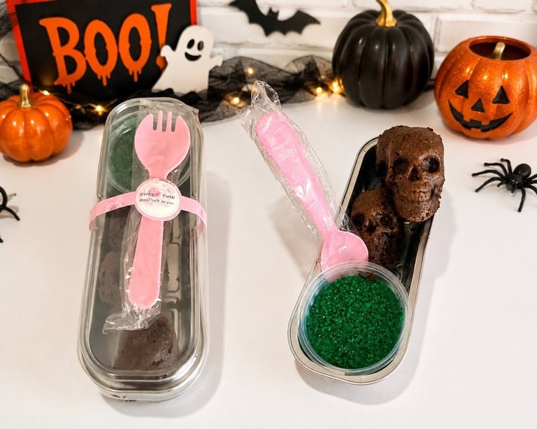 Halloween-themed chocolate treats with pink spoons surrounded by decorative pumpkins, bats, and BOO sign