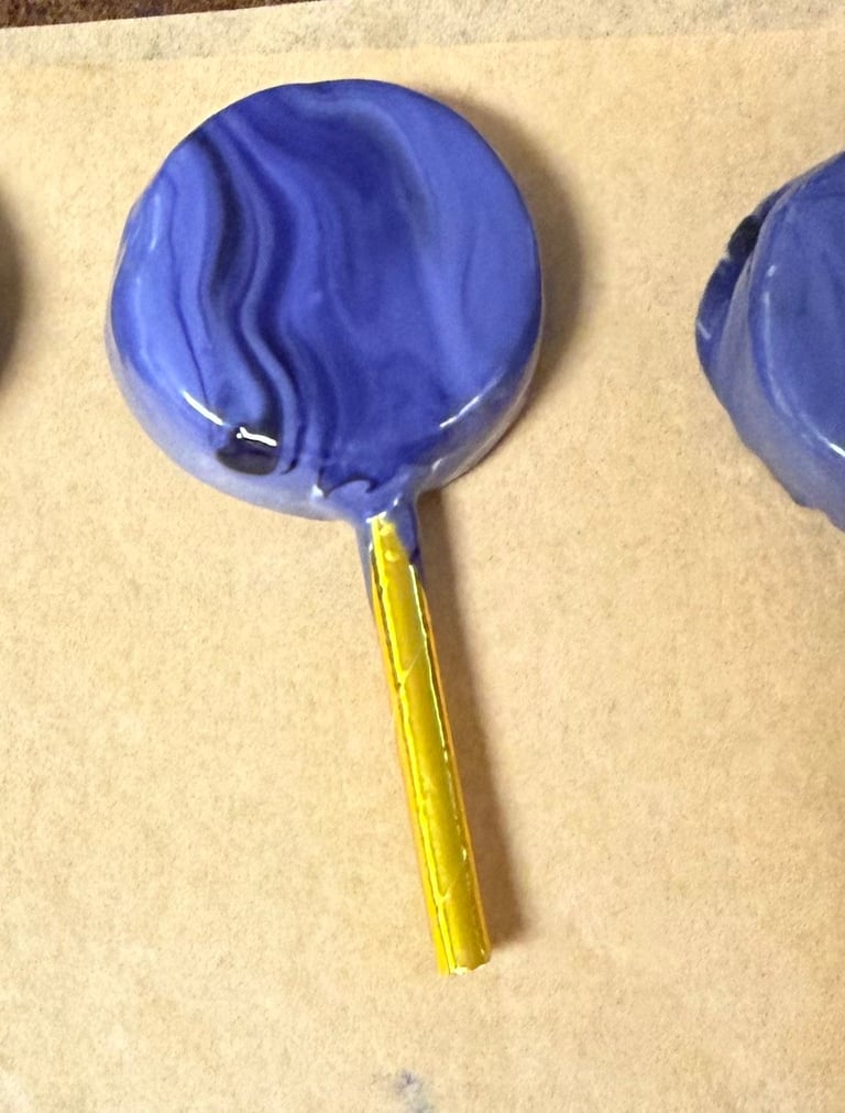 Blue round lollipop with swirl pattern and yellow stick on beige surface