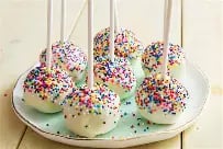 Cake pops decorated with colorful sprinkles on white sticks arranged on a mint green plate