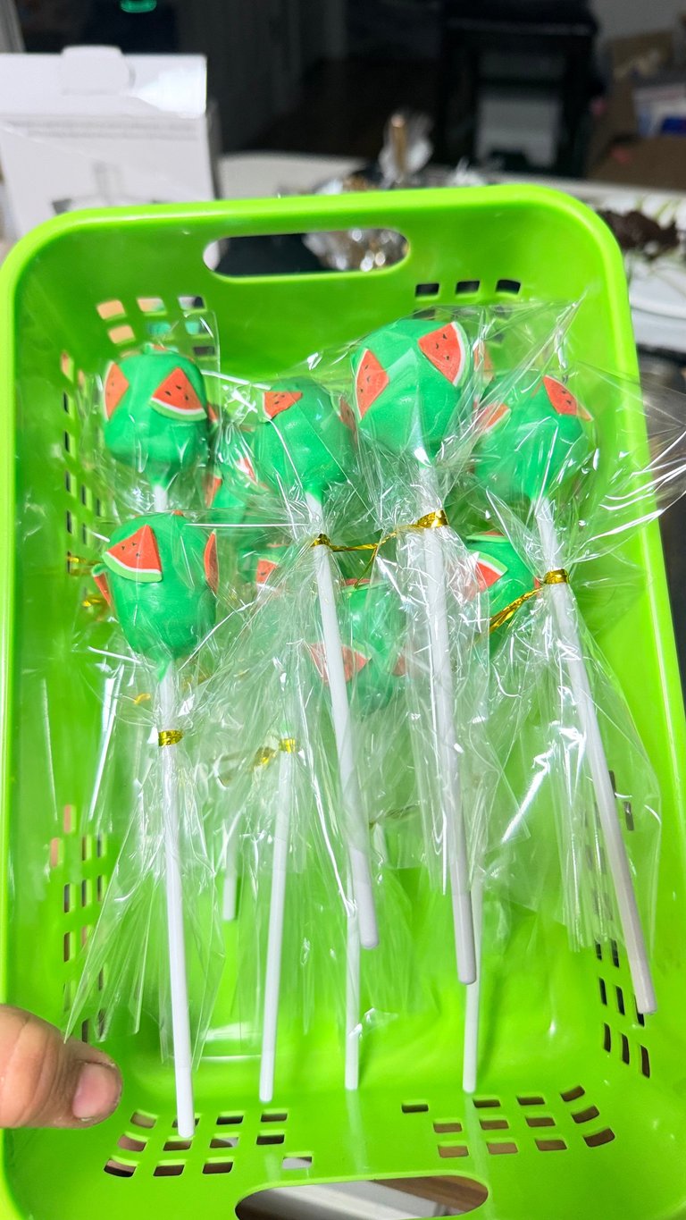 Bright green plastic basket containing wrapped watermelon lollipops with red and green designs on white sticks