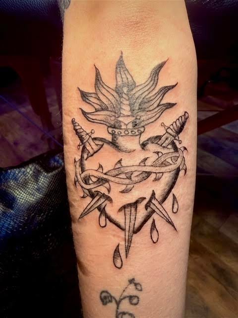 Black and gray tattoo on an arm featuring a crowned spiky plant or succulent design with ornamental swords and decorative elements