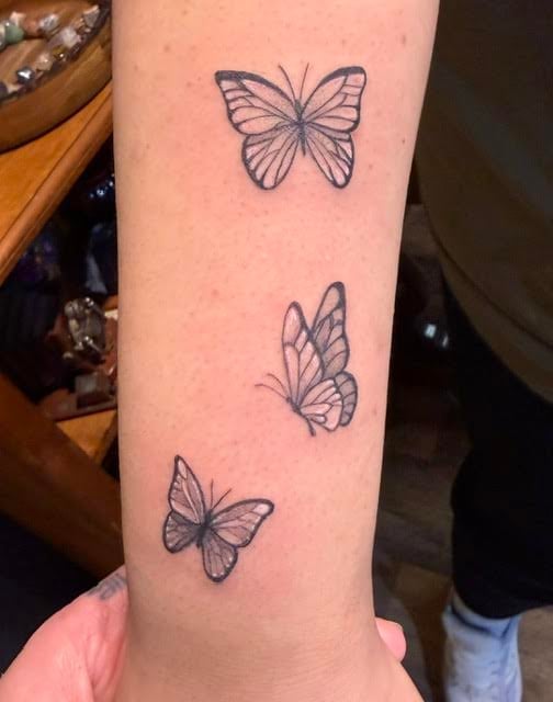 Three delicate butterfly tattoos arranged vertically on a persons arm in black line work