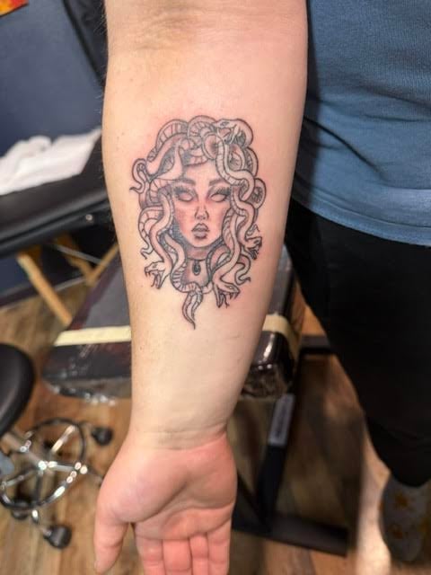 Medusa head tattoo on forearm featuring a female face with snake hair in black ink