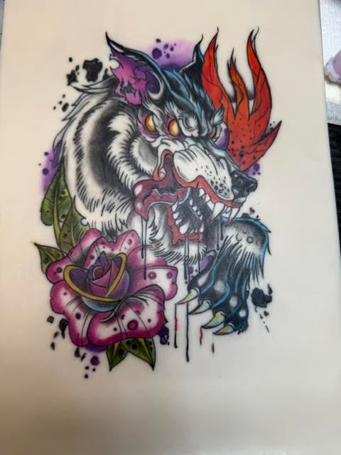 Colorful tattoo design featuring a fierce wolf head with red flames, purple watercolor accents, and pink roses with green leaves