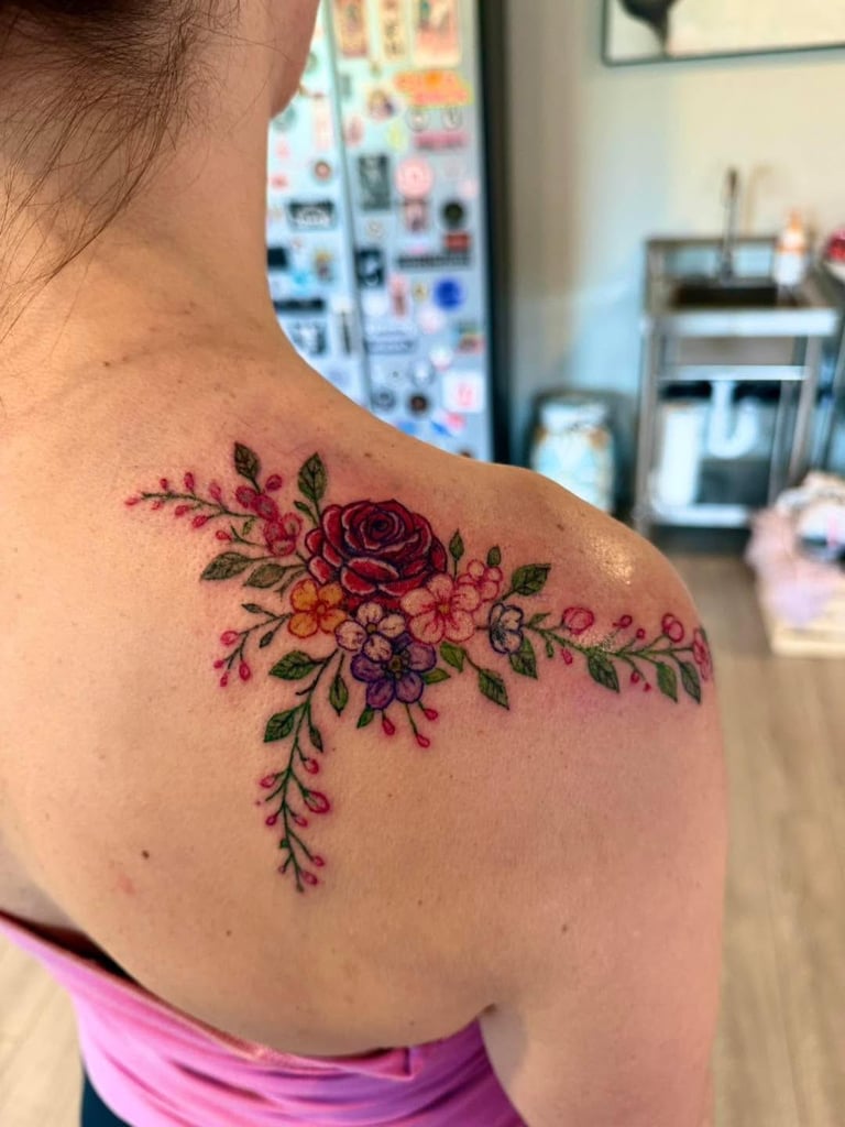 Colorful floral tattoo on shoulder featuring red roses and small purple and yellow flowers with green leaves