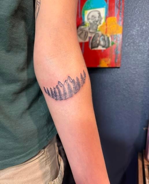 Person wearing a green shirt displaying a mountain range tattoo on their forearm