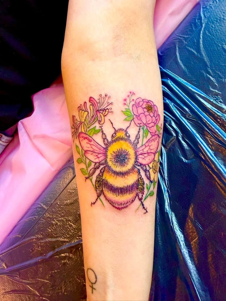 Colorful bee and flower tattoo on forearm featuring a bumblebee with pink and yellow blooms in vibrant inks