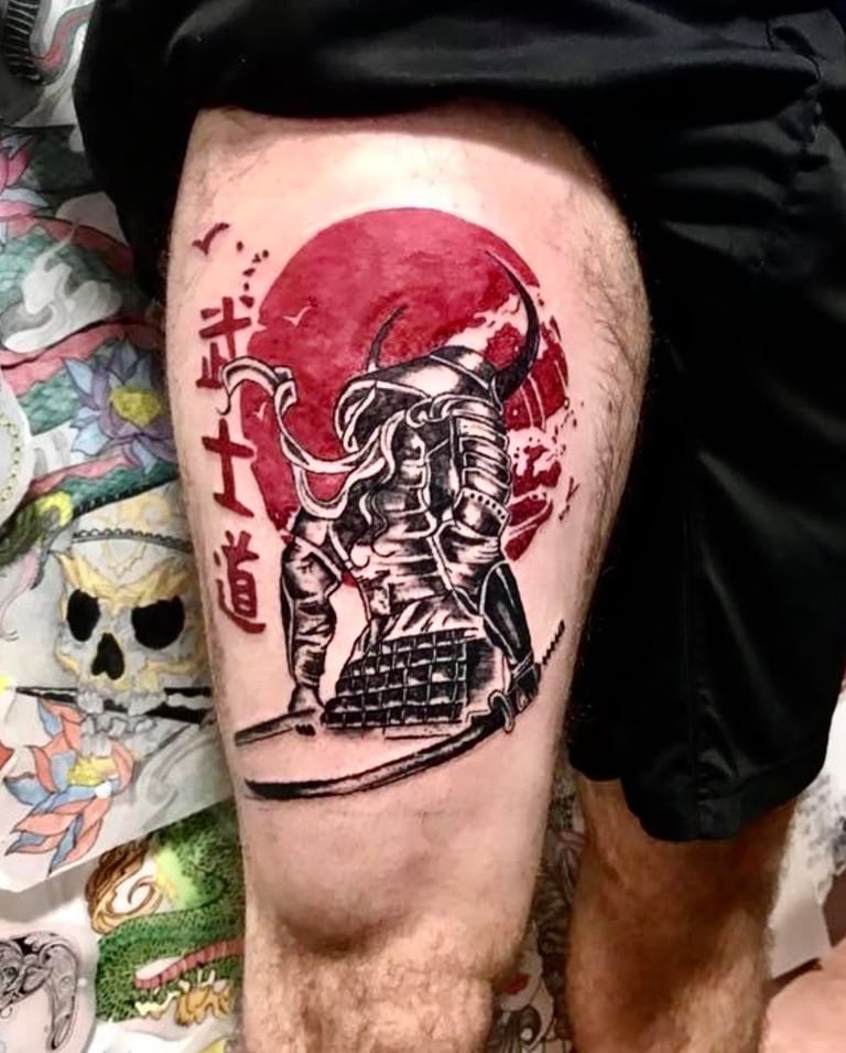 Tattoo of samurai warrior in armor with red moon and Japanese characters on persons thigh