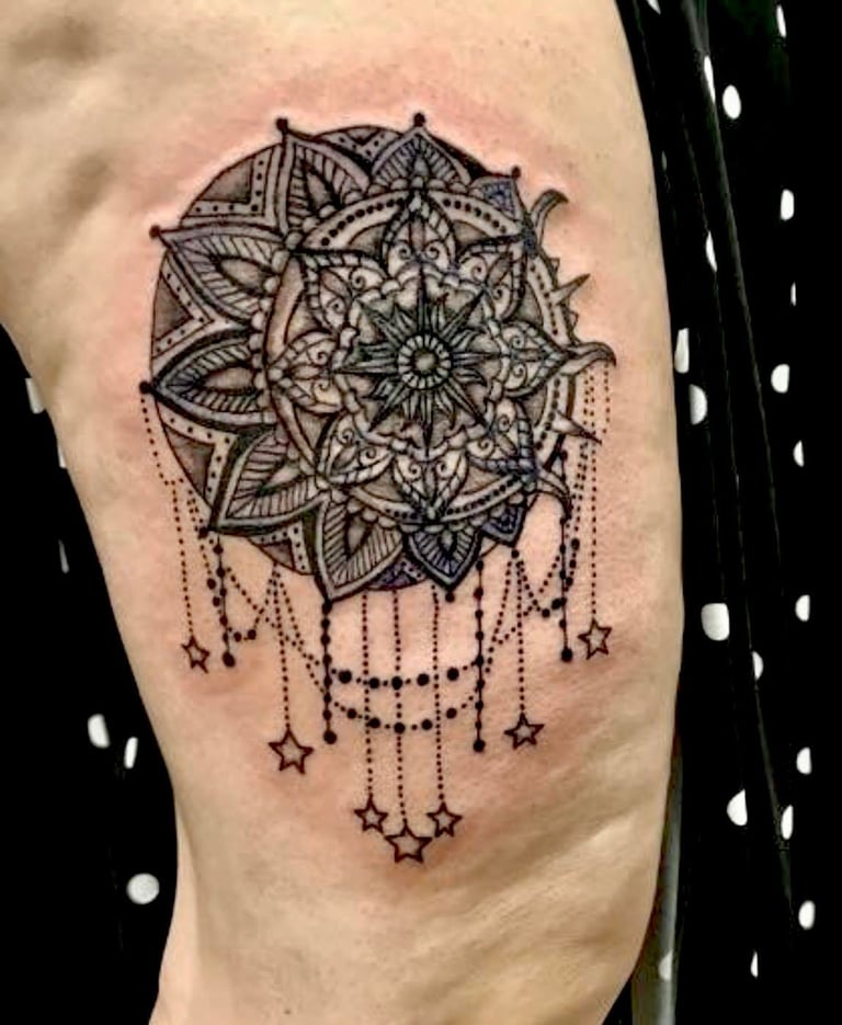 Black ink mandala tattoo on thigh with intricate geometric patterns and hanging stars and dot details