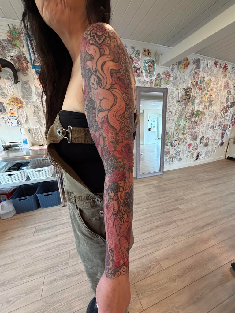 Person displaying a full-length red and black ornamental tattoo sleeve on their arm in a studio with artwork on walls