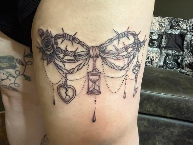 Ornate line tattoo on thigh featuring draped roses, thorns, chains, hourglass, and hanging heart pendant