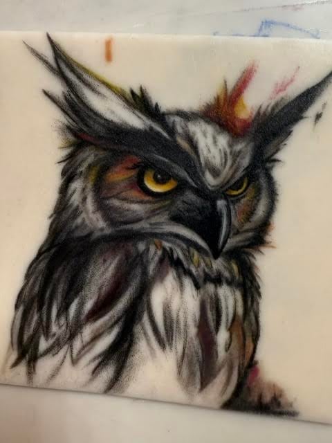 Colored pencil drawing of an owl with intense yellow eyes, black and white feathers, and pointed ear tufts on cream paper