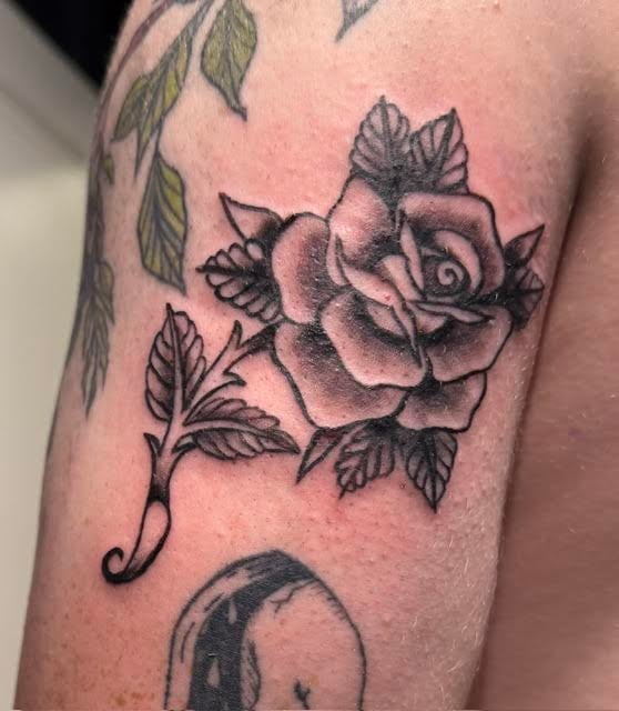 Black and gray rose tattoo with leaves on a persons upper arm and shoulder