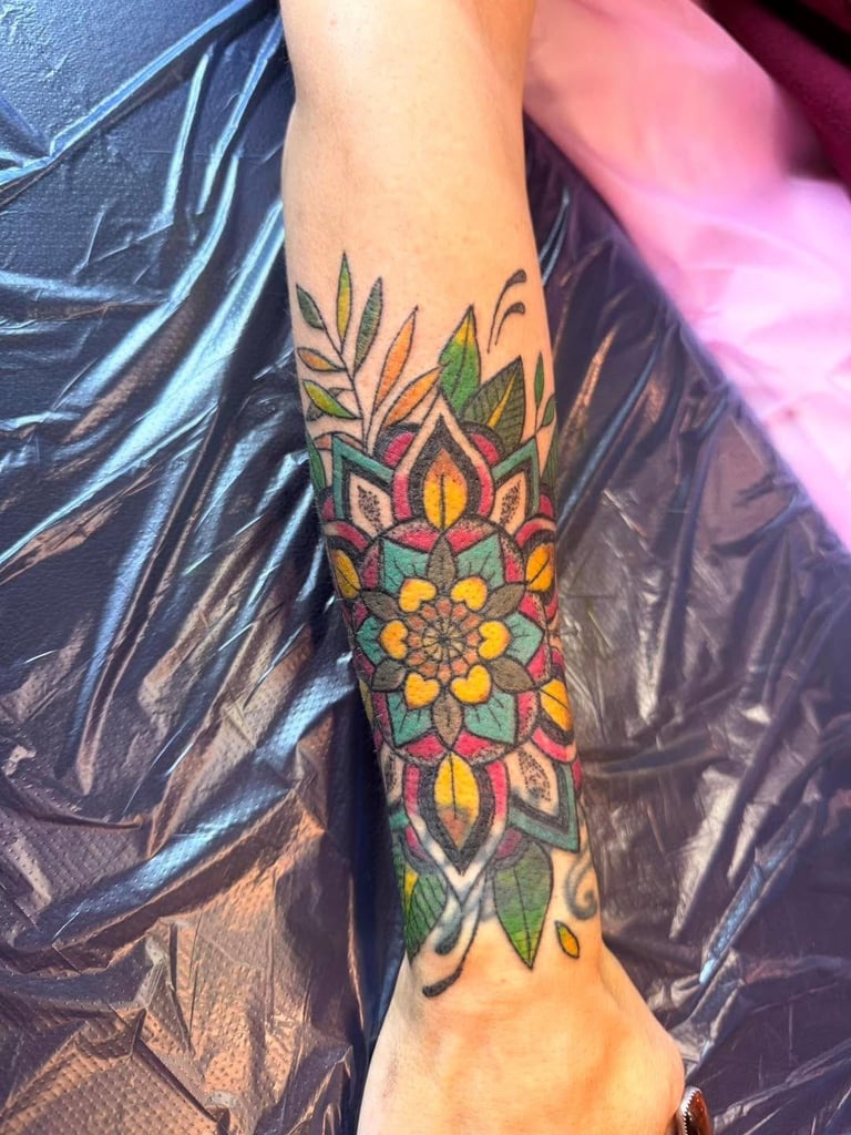 Colorful mandala tattoo on forearm featuring vibrant geometric patterns in red, yellow, green, and orange hues