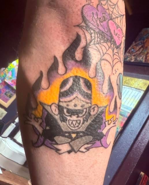 Colorful tattoo on arm featuring a demonic face with horns surrounded by yellow flames and purple spider web designs