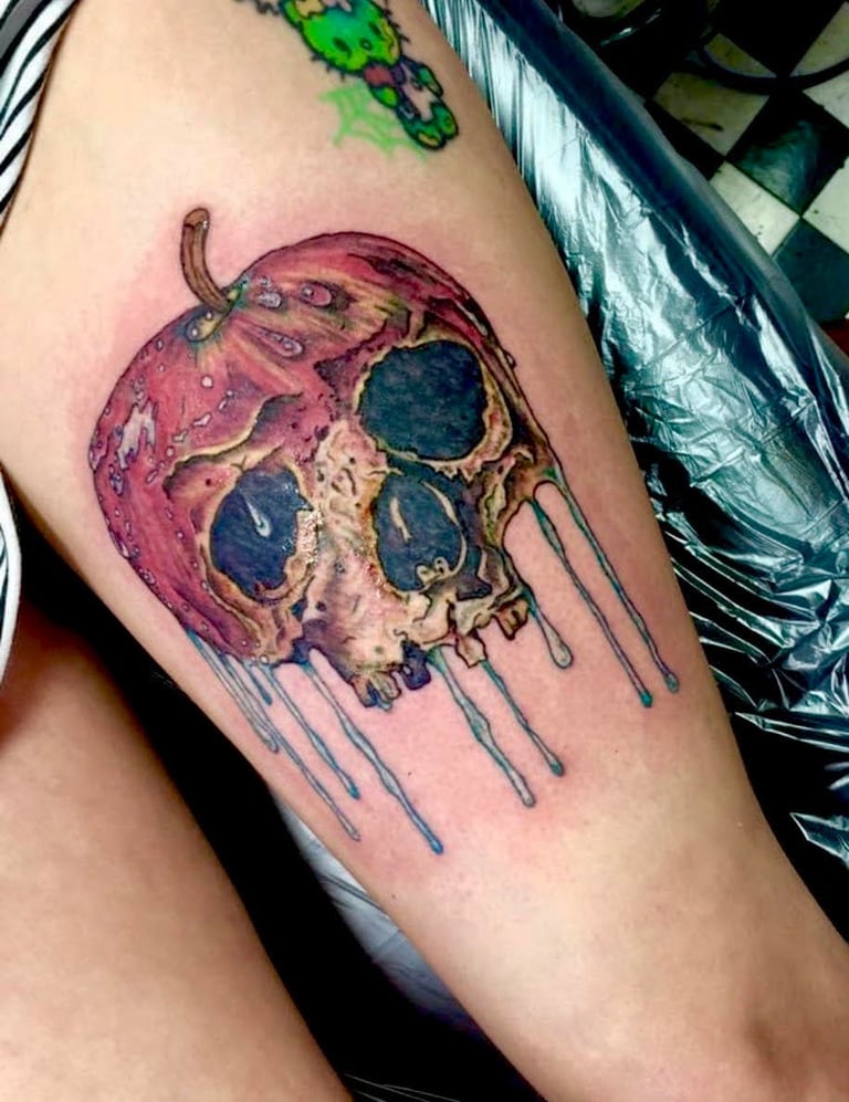 Colorful tattoo of a melting red and purple skull with dripping paint streaks on a persons thigh
