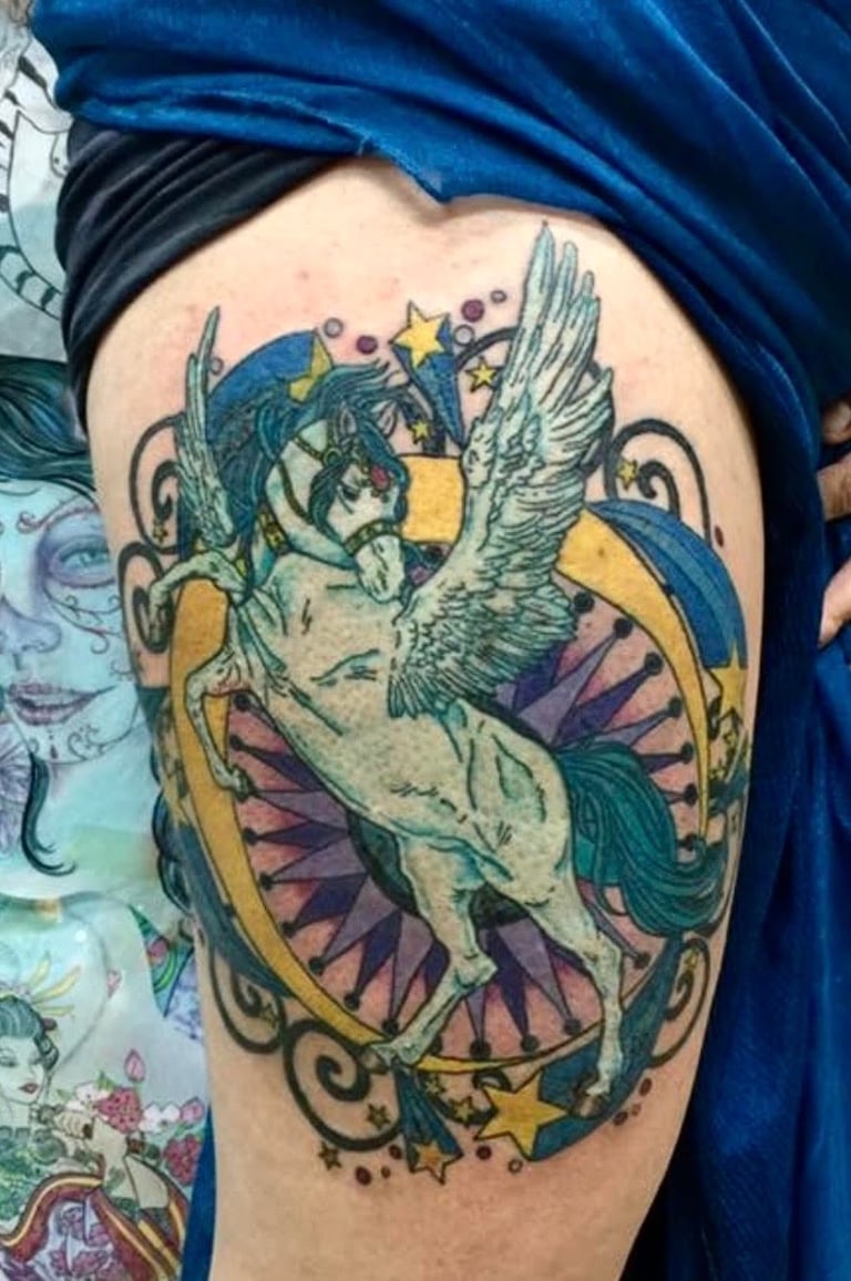 Colorful tattoo of a winged mermaid with blue and green tones, yellow stars, and purple shell motifs on upper arm