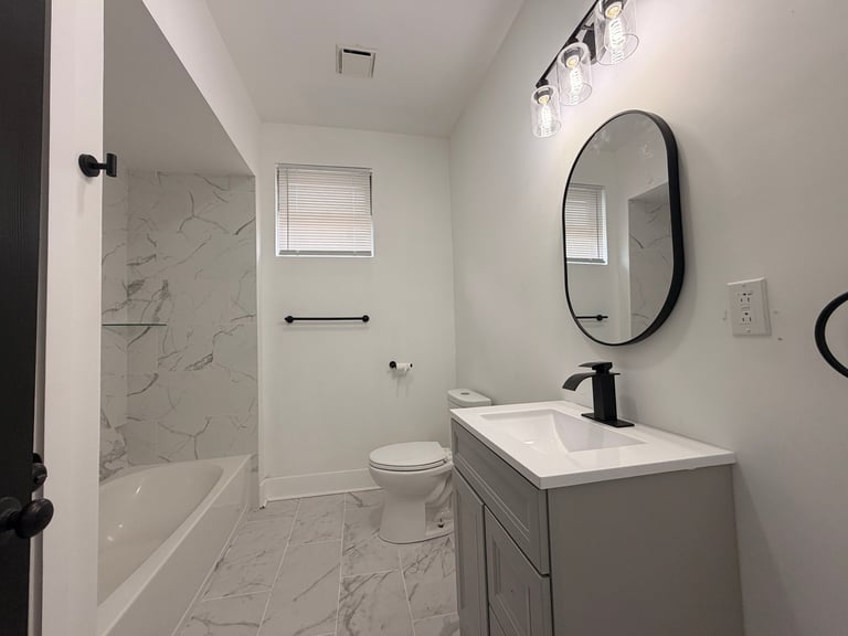 Modern bathroom with marble shower enclosure, gray vanity, oval mirror, and white tile flooring