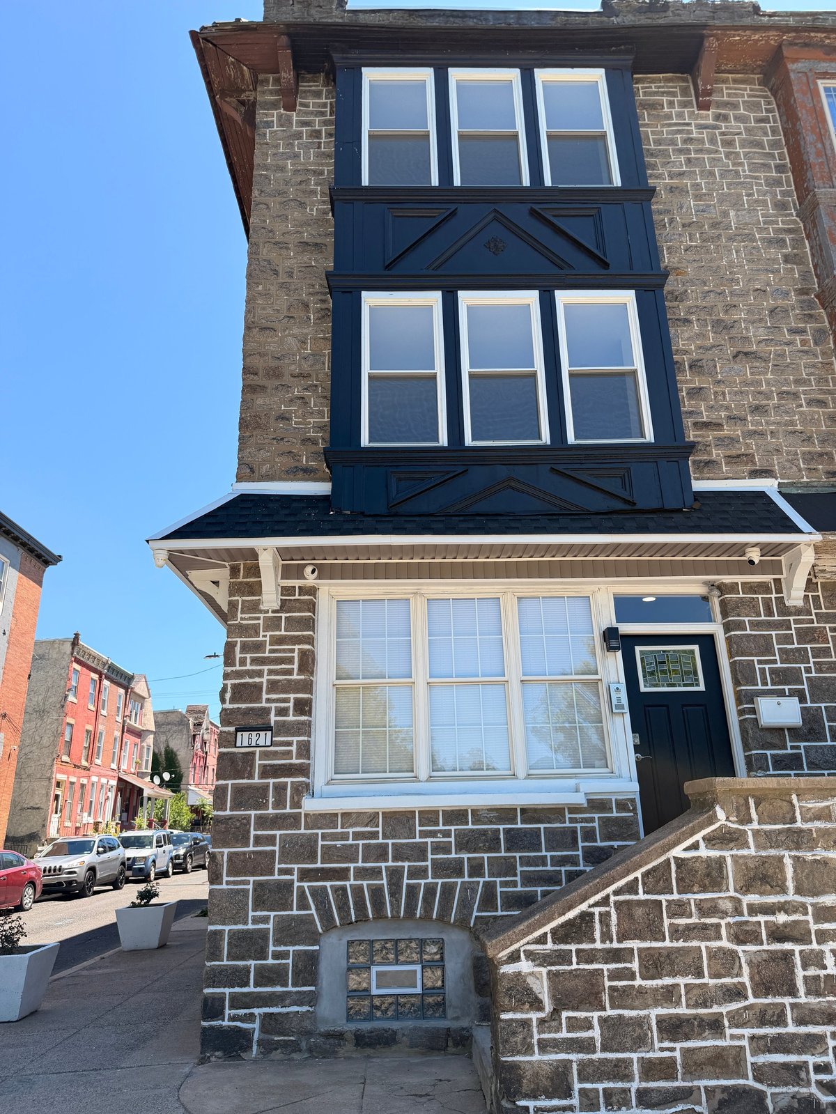 Front facade of a historic stone townhouse with blue-framed windows, cream-colored ground floor windows, and a street view