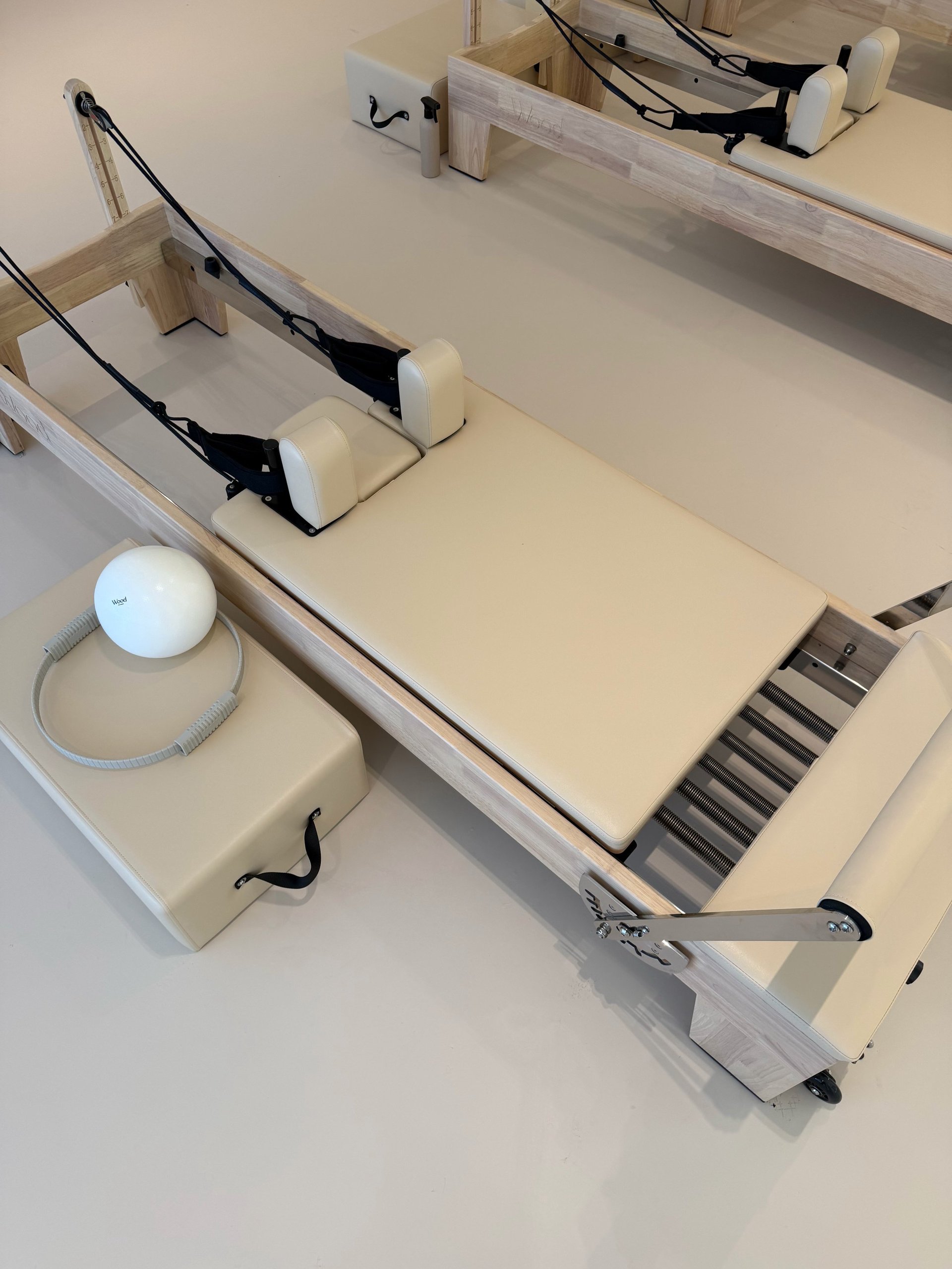 Two cream-colored Pilates reformer machines with footbars, springs, and adjustable headpieces set up in a studio