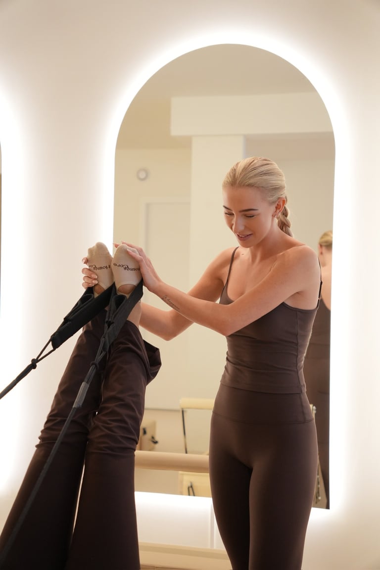 Woman in brown dress adjusting another womans collar in an archway with illuminated mirror