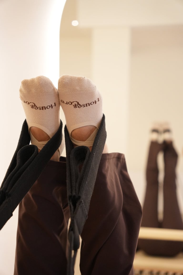 Persons feet wearing cream-colored socks with text and open-toed brown sandals, held up against a beige interior background