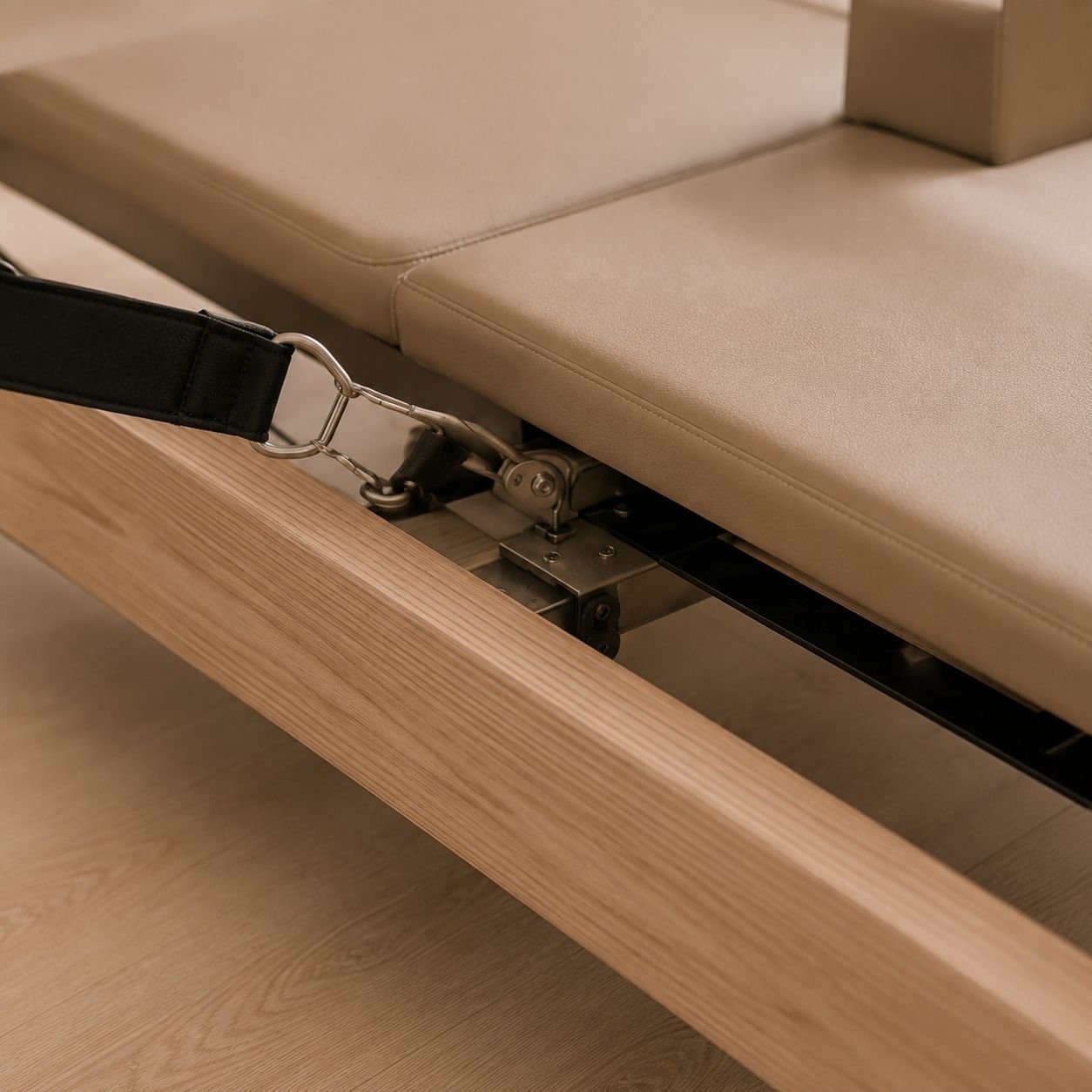 Underside of a tan upholstered bed frame showing wooden base and metal adjustment mechanism with black straps