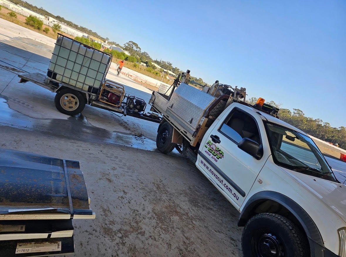 White pickup truck parked on wet pavement with livestock trailers and industrial area in background