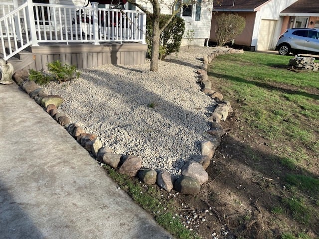 Residential yard showing gravel landscaping bordered by landscape rocks next to a concrete patio and white deck