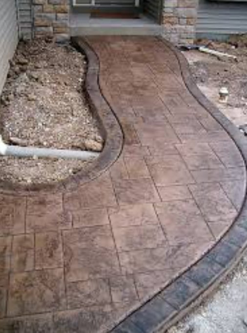 Curved brown decorative concrete patio with stone edging next to landscaping area of a residential property