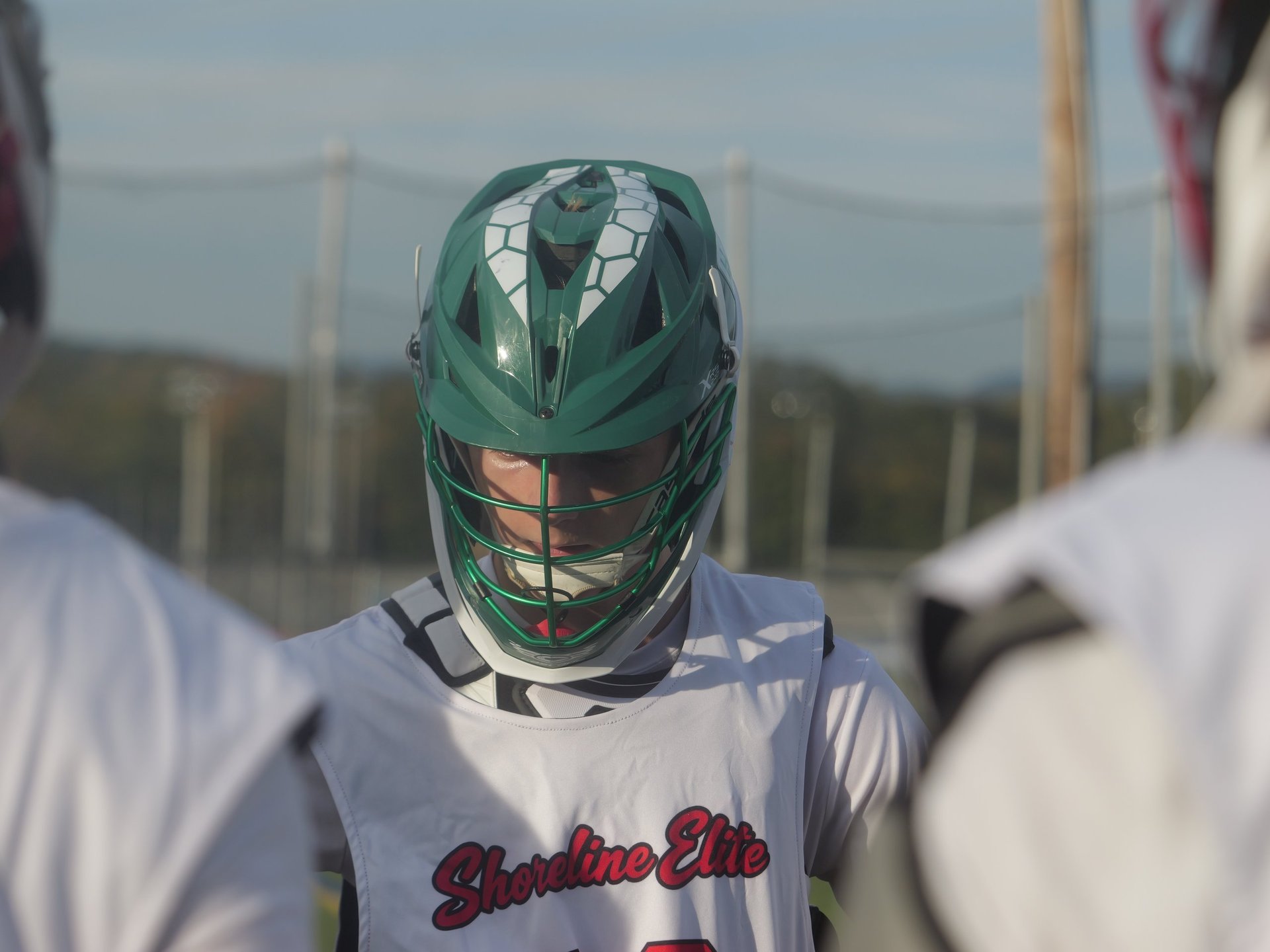 Lacrosse player wearing a green helmet and white jersey with a Cardinal logo during an outdoor game