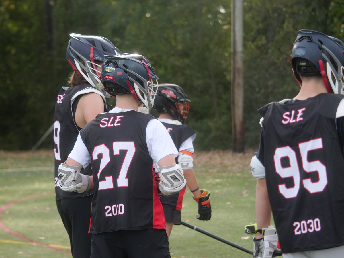 Youth lacrosse players in black jerseys numbered 27 and 95 standing together with helmets and equipment