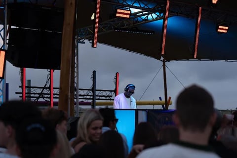 Speaker at outdoor event podium with crowd in foreground and industrial stage structure overhead