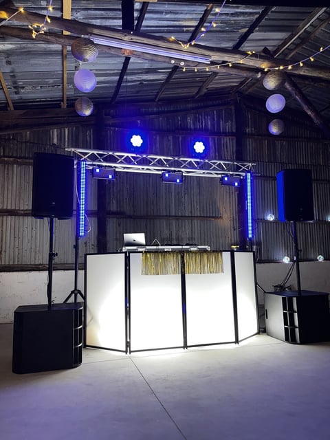Professional DJ booth with white panels and gold fringe inside an industrial warehouse venue with blue stage lighting