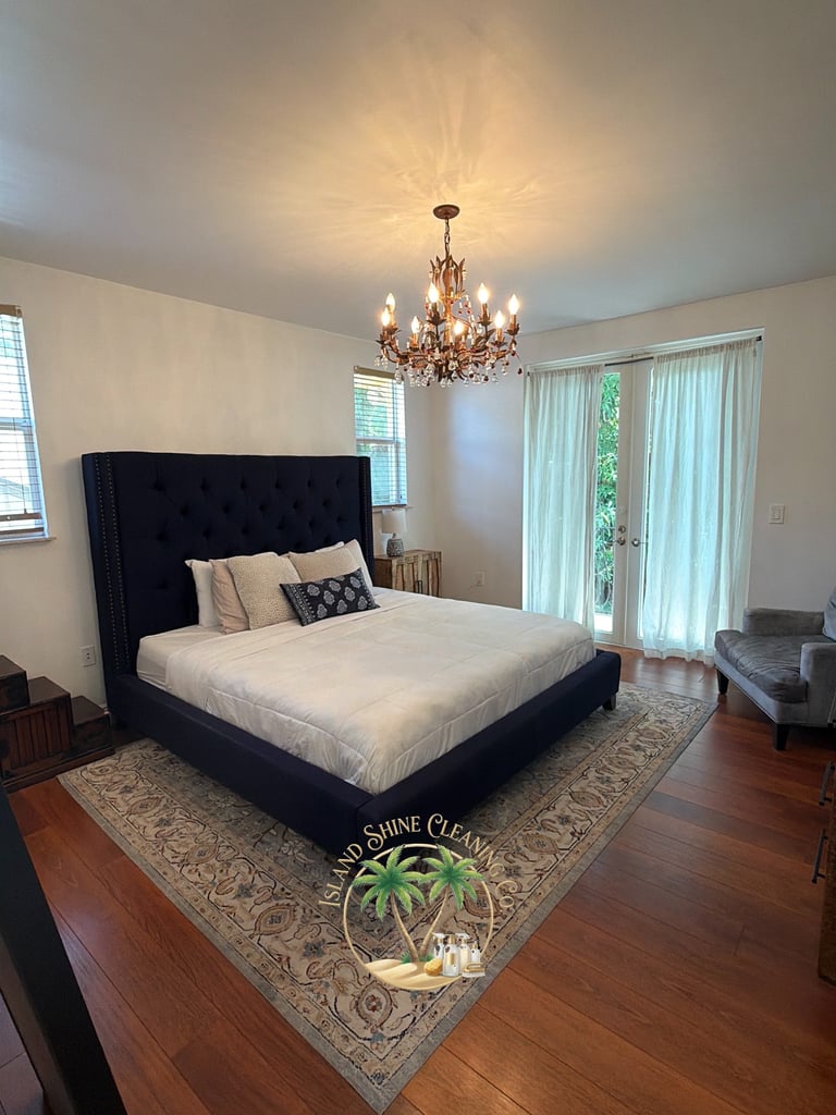 Modern bedroom with black tufted bed, ornate chandelier, hardwood floors, and glass doors opening to patio area