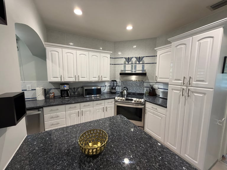 Modern kitchen with white cabinets, dark granite countertop, stainless steel appliances, and a gold decorative bowl on the counter
