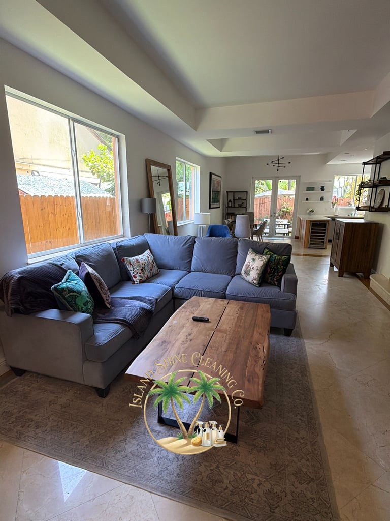 Bright living room with blue sectional sofa, wooden coffee table, and large windows overlooking a yard