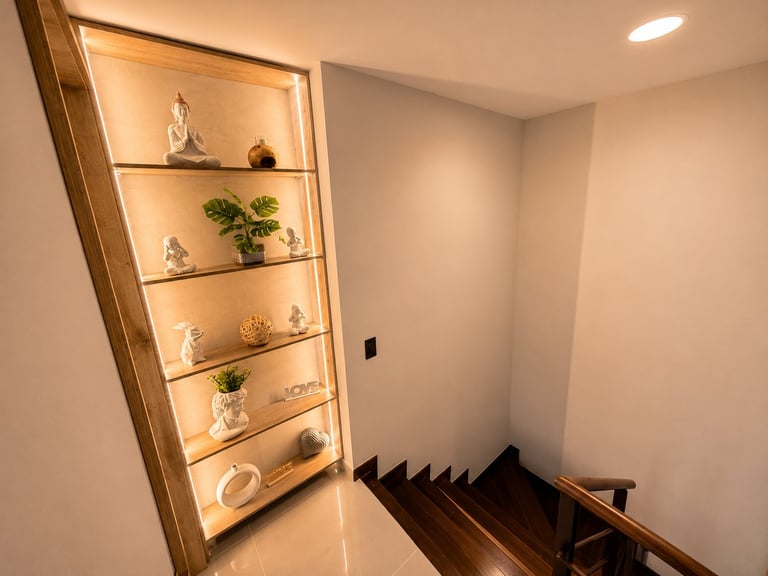 Illuminated wooden display cabinet with shelves holding decorative items and plants beside a staircase with dark wooden steps