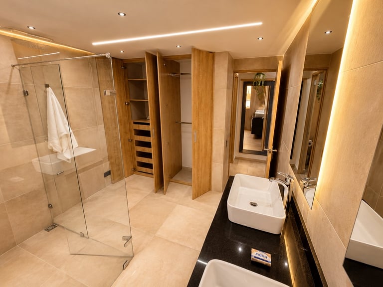 Modern luxury bathroom with double vanity sinks, glass shower enclosure, wooden cabinetry, and warm ceiling lights.