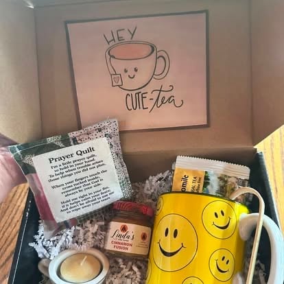Cute tea gift box containing yellow smiley face mug, tea bags, prayer guide, honey jar, and decorative sign reading Hey Cute tea