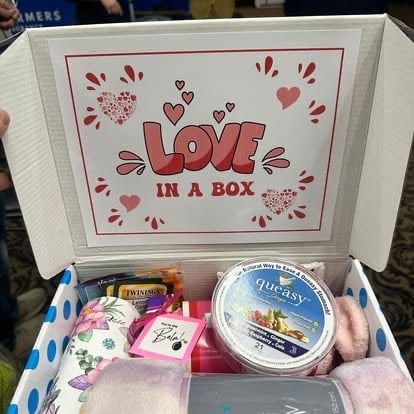 Open gift box labeled Love in a Box containing tea, candles, bath items, and decorative treats with heart designs