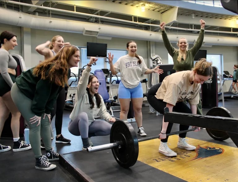 Group of people in gym watching woman lift barbell during fitness class with celebratory atmosphere