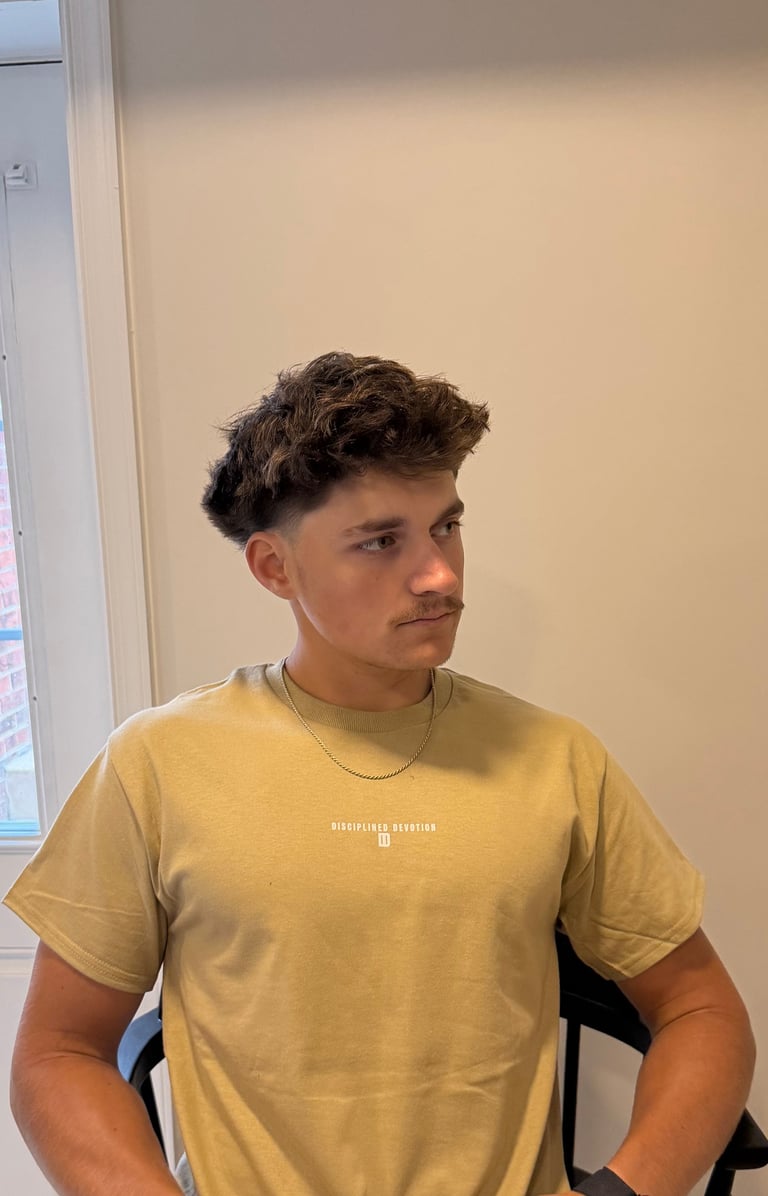 Young man with dark wavy hair wearing a mustard yellow Disciplined Devotion monogram t-shirt