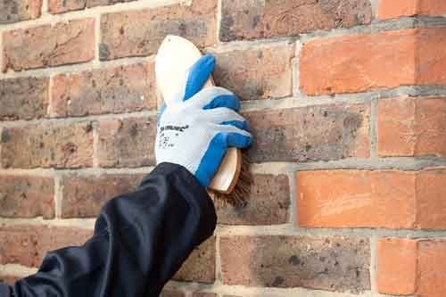 Hand in blue and white glove cleaning brick wall with cloth