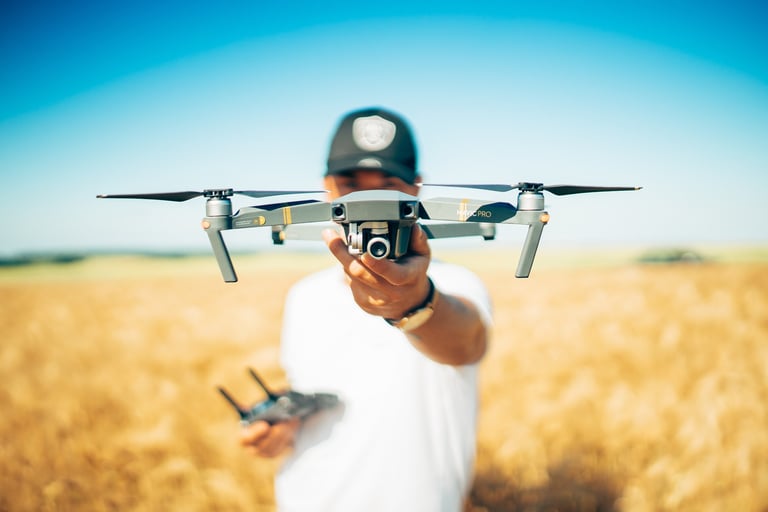 Man in white shirt and orange cap holding drone above his head in a golden wheat field under blue sky