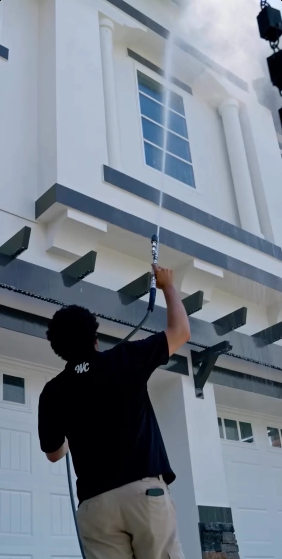 Person in black shirt reaching up to adjust an antenna or cable on the exterior of a white and dark blue modern house