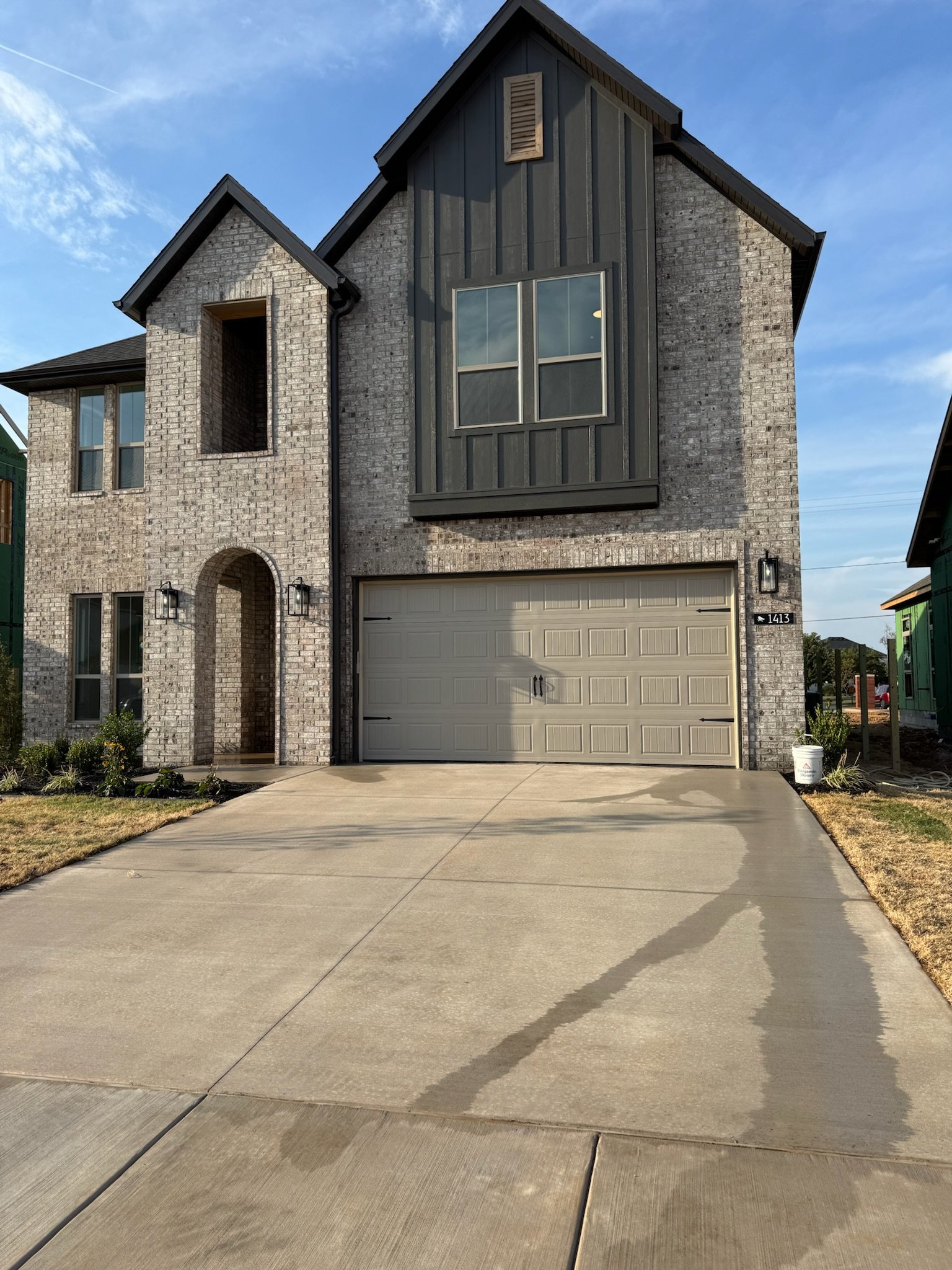Modern two-story brick home with black metal siding, gray garage door, and concrete driveway under blue sky