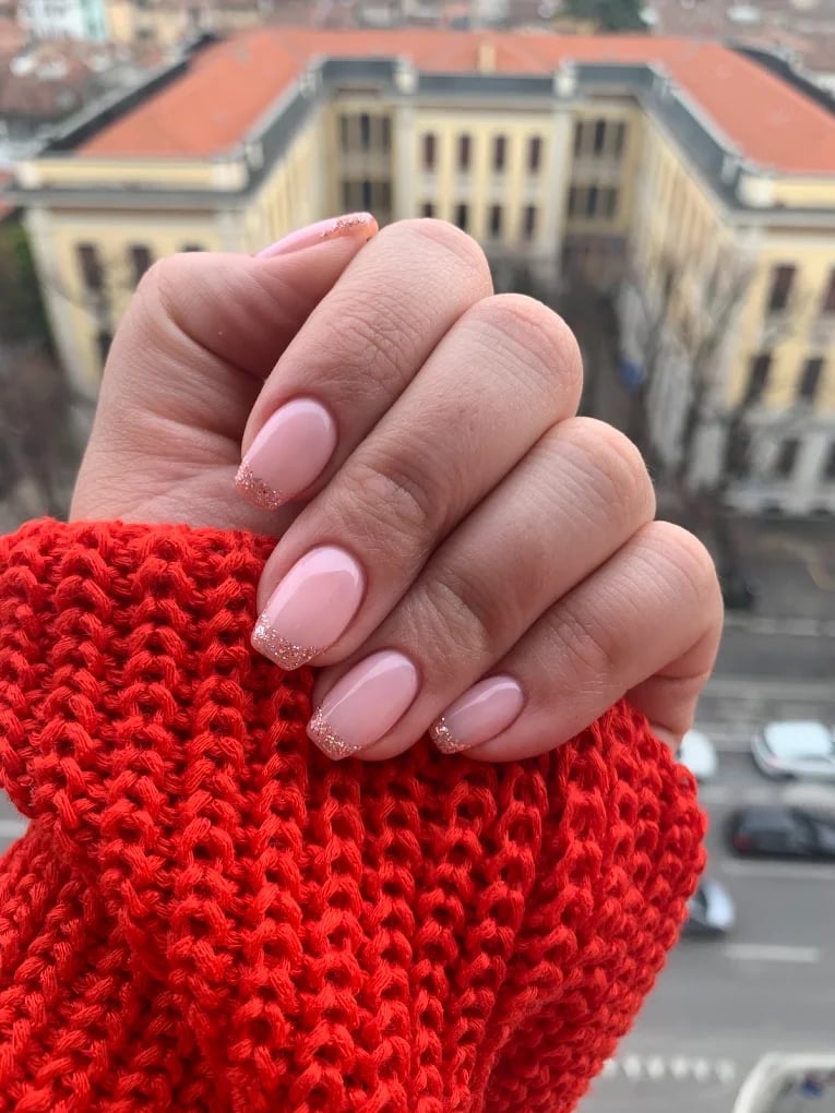 Manicure rosa con glitter su mano con maglia rossa