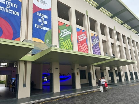 Modern educational building with colorful banners about learning and education, featuring blue glass entrance and a person standing outside